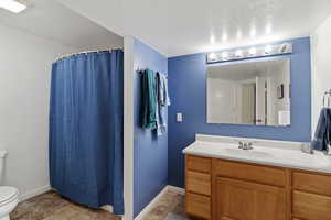 Full bath featuring toilet, baseboards, vanity, and a textured ceiling