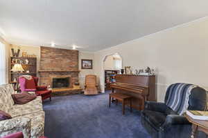 Living room featuring crown molding, dark carpet, a textured ceiling, a brick fireplace, and arched walkways