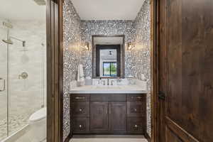 Bathroom with a stall shower, vanity, toilet, and wallpapered walls