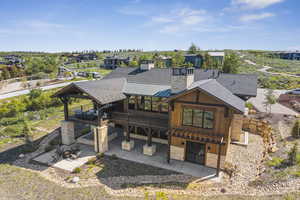 Rear view of property with stone siding, a patio, a deck, a chimney, and a shingled roof