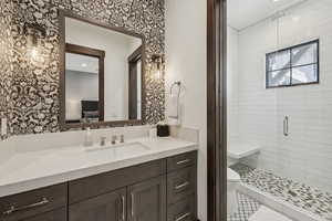 Ensuite bathroom with vanity, wallpapered walls, a stall shower, and toilet