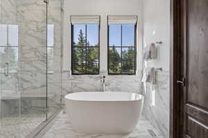 Full bath featuring a freestanding tub, marble finish flooring, a marble finish shower, and tile walls