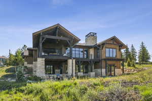 Rear view of property featuring stone siding, a balcony, and a chimney