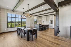 Dining room featuring light wood-type flooring, beamed ceiling, a chandelier, baseboards, and wallpapered walls