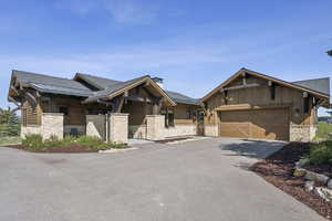 View of front of property with stone siding, asphalt driveway, a garage, and roof with shingles