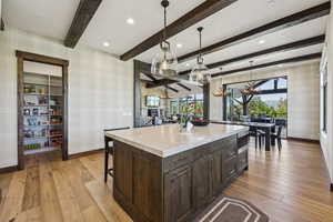 Kitchen with wallpapered walls, baseboards, a chandelier, light wood-style flooring, and beamed ceiling