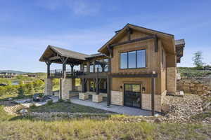 Rear view of house with a patio area, stone siding, and a wooden deck