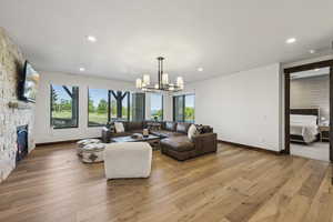 Living room featuring a chandelier, a fireplace, baseboards, light wood finished floors, and recessed lighting