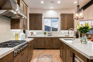 Kitchen with wall chimney exhaust hood, stainless steel gas stovetop, light countertops, light wood-style floors, and tasteful backsplash