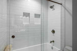 Full bath featuring combined bath / shower with glass door and toilet