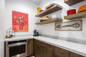 Kitchen featuring open shelves, oven, light countertops, and dark brown cabinetry