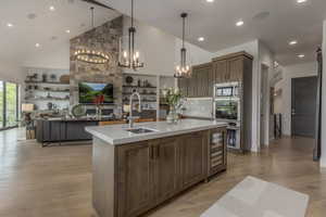Kitchen featuring high vaulted ceiling, a kitchen island with sink, light countertops, light wood-style floors, and stainless steel appliances