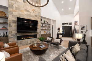 Living area with built in shelves, high vaulted ceiling, wood finished floors, a stone fireplace, and recessed lighting