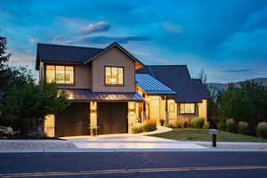 View of front of home featuring a standing seam roof, driveway, a garage, a metal roof, and stone siding