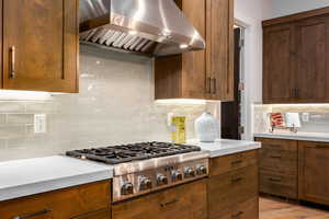 Kitchen featuring wall chimney range hood, stainless steel gas stovetop, backsplash, light countertops, and light wood-type flooring