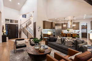 Living room with a chandelier, light wood-type flooring, high vaulted ceiling, stairway, and recessed lighting
