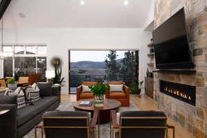 Living area featuring light wood finished floors, a stone fireplace, recessed lighting, and vaulted ceiling