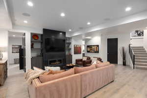 Living room featuring light wood-type flooring, recessed lighting, a fireplace, stairs, and built in features