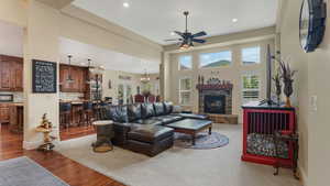 Living area with ceiling fan, recessed lighting, dark wood-style flooring, a stone fireplace, and a towering ceiling