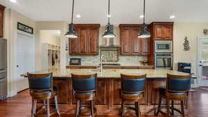 Kitchen with stainless steel appliances, a sink, tasteful backsplash, dark wood-style floors, and a center island with sink