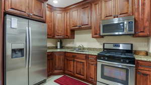 Kitchen with stainless steel appliances, a sink, light stone countertops, and light tile patterned floors