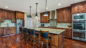 Kitchen with stainless steel appliances, wall chimney range hood, a sink, decorative backsplash, and recessed lighting