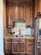 Kitchen featuring stainless steel fridge with ice dispenser, a sink, decorative backsplash, and light stone countertops