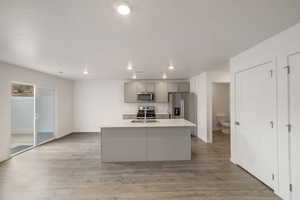 Kitchen featuring appliances with stainless steel finishes, gray cabinets, light countertops, a center island with sink, and recessed lighting
