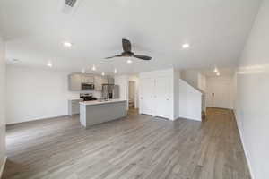 Kitchen with stainless steel appliances, open floor plan, baseboards, recessed lighting, and a kitchen island with sink