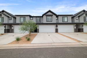 Townhome / multi-family property with stucco siding, an attached garage, stone siding, and driveway