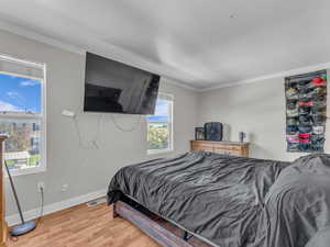 Bedroom with baseboards, light wood-style flooring, and crown molding