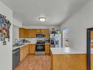 Kitchen featuring stainless steel appliances, a sink, light wood-type flooring, light countertops, and a peninsula