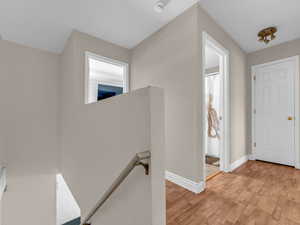 Corridor with an upstairs landing, light wood finished floors, and baseboards