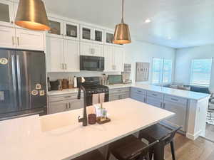 Kitchen with black appliances, a peninsula, wood finished floors, light countertops, and glass insert cabinets