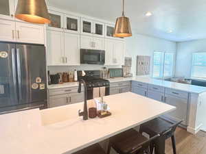 Kitchen with black appliances, a peninsula, wood finished floors, light countertops, and glass insert cabinets