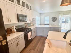 Kitchen featuring stainless steel microwave, range with gas cooktop, freestanding refrigerator, light countertops, and wood finished floors