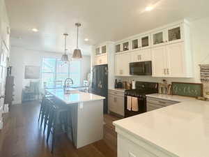 Kitchen featuring black appliances, recessed lighting, dark wood finished floors, an island with sink, and white cabinets