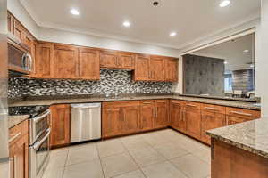 Kitchen featuring stainless steel appliances, a sink, brown cabinets, dark stone counters, and recessed lighting