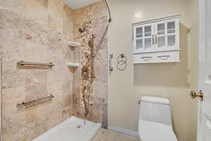 Full bathroom featuring tiled shower, toilet, tile patterned flooring, and baseboards