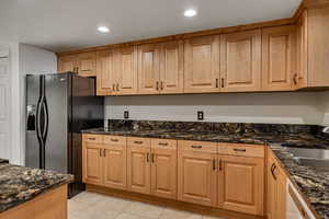 Kitchen with black refrigerator with ice dispenser, a sink, dark stone countertops, light tile patterned floors, and recessed lighting