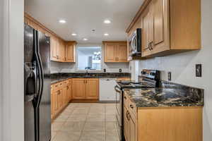 Kitchen featuring black fridge with ice dispenser, electric stove, white dishwasher, stainless steel microwave, and a sink