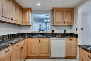 Kitchen with dishwasher, a sink, dark stone countertops, a chandelier, and light brown cabinetry