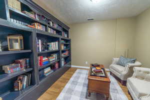 Living area with wood finished floors, a textured ceiling, and baseboards