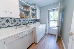 Laundry area featuring separate washer and dryer, cabinet space, light wood-style flooring, and baseboards