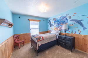 Carpeted bedroom featuring wainscoting, wooden walls, and a textured ceiling