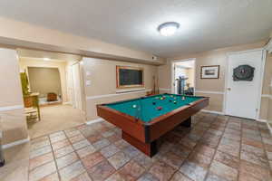 Recreation room featuring light stone finish flooring, billiards, a textured ceiling, and baseboards