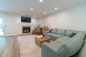 Living room with light wood-type flooring, a tiled fireplace, recessed lighting, and baseboards