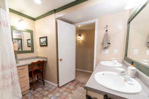 Bathroom with double vanity, stone finish flooring, and baseboards