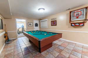 Recreation room with a textured ceiling, baseboards, billiards, and stone finish flooring