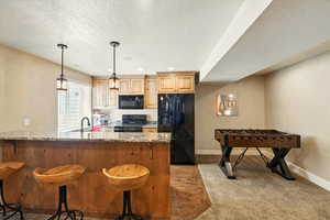 Kitchen featuring black appliances, a sink, a textured ceiling, light stone counters, and baseboards